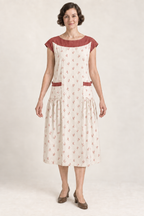 AI design illustration of the same yoke apron dress in ivory with muted brick-red sprigs and contrast yoke, front view