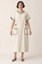 AI design illustration of the same cream bungalow apron dress with leaf-green edging and side tabs, front view
