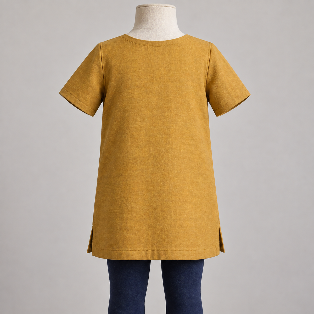 AI design preview: rear of ochre-gold child tunic with shallow faced neckline, plain continuous back and short set-in sleeves