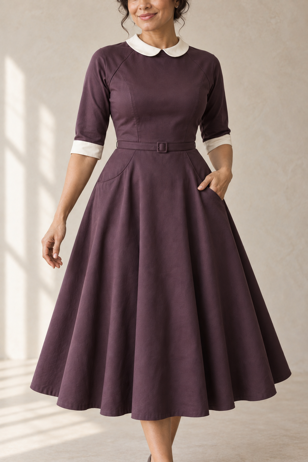 Closer front design preview of the aubergine raglan dress rounded collar, closed bodice, waist belt and curved yoke-seam pockets.