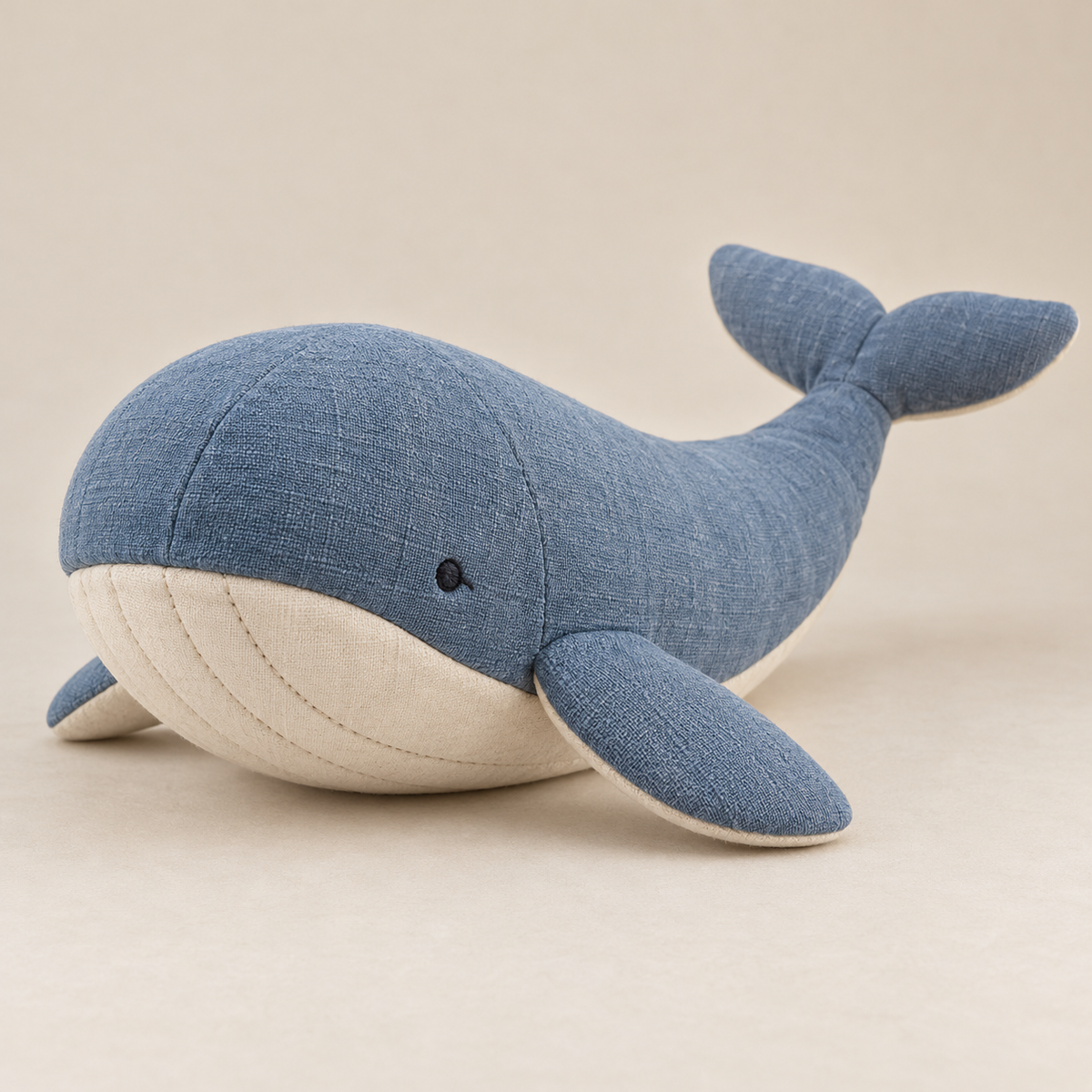 Blue woven-fabric whale plush with ivory belly, rounded flippers and embroidered eyes, front view