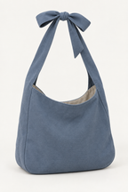 AI design preview: slate-blue shoulder bag with a functional bow joining the broad fabric strap ends