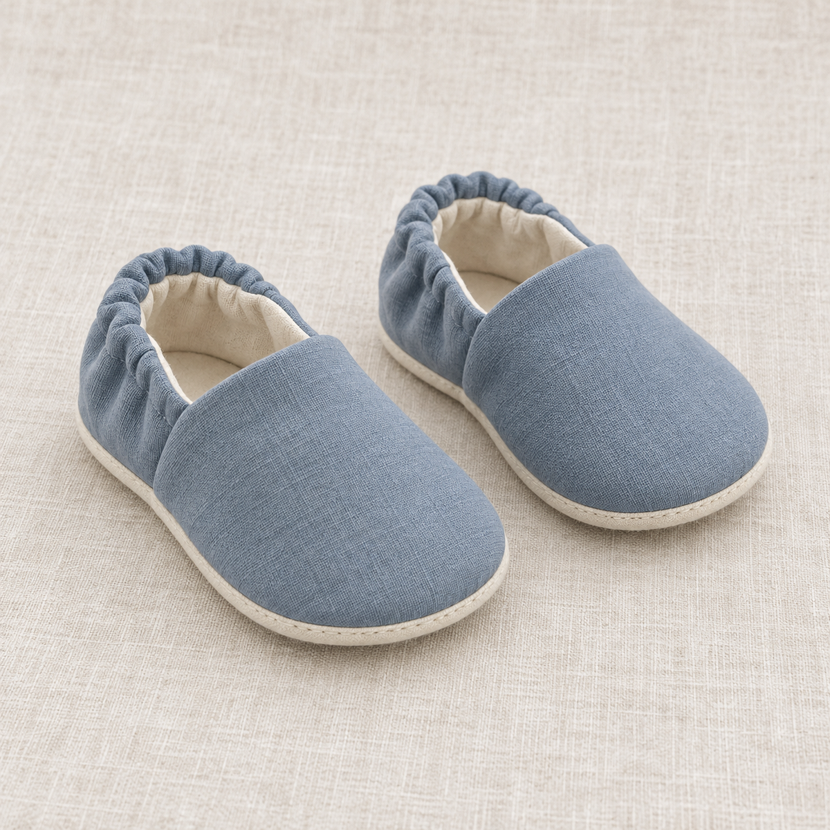 AI design preview: slate-blue soft baby shoes with rounded vamps, gathered elastic heels and cream lining, front view