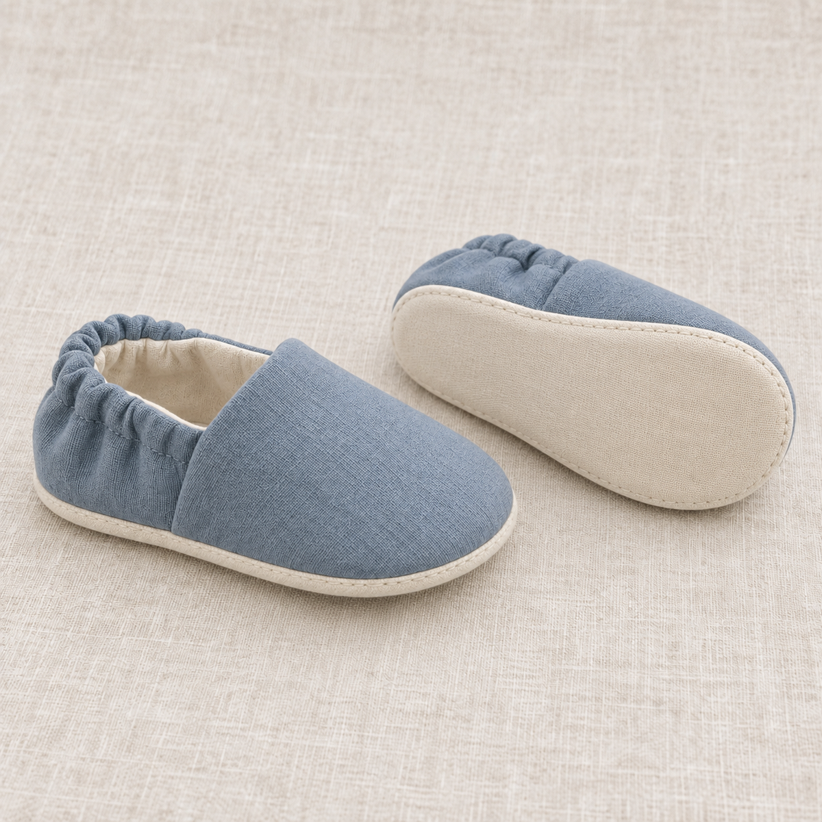 AI design preview: same slate-blue baby shoes in side and sole views, showing a plain cream flexible textile sole
