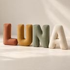 Stuffed fabric letters spelling LUNA in terracotta, ochre, sage and ivory, shown from the front