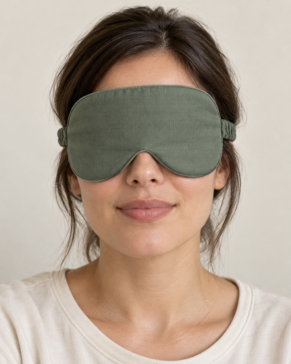 Design preview: adult woman wearing a plain sage green fabric sleep mask with curved lower lobes, a nose notch and a fabric-covered elastic strap