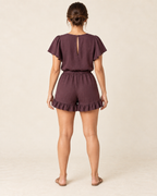 AI design preview: rear of the same aubergine romper, showing narrow back keyhole, elastic waist and two ruffled leg hems