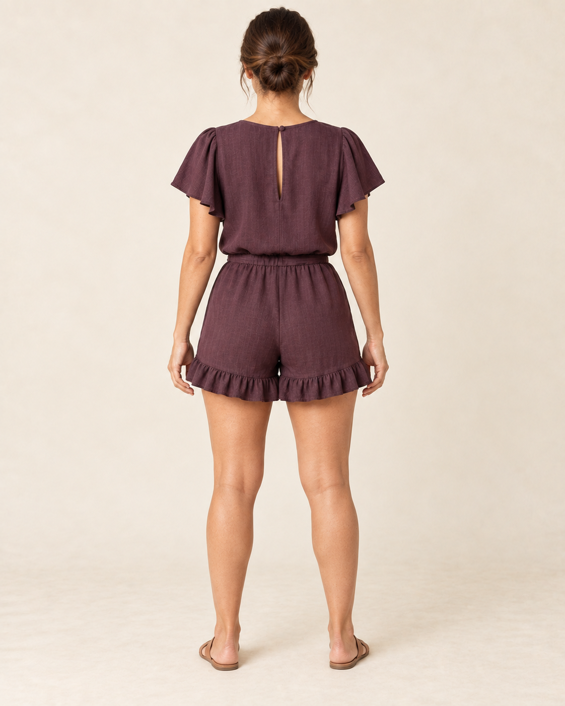 AI design preview: rear of the same aubergine romper, showing narrow back keyhole, elastic waist and two ruffled leg hems
