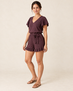 AI design preview: three-quarter view of the same woman in the aubergine flutter-sleeve romper with a self tie sash