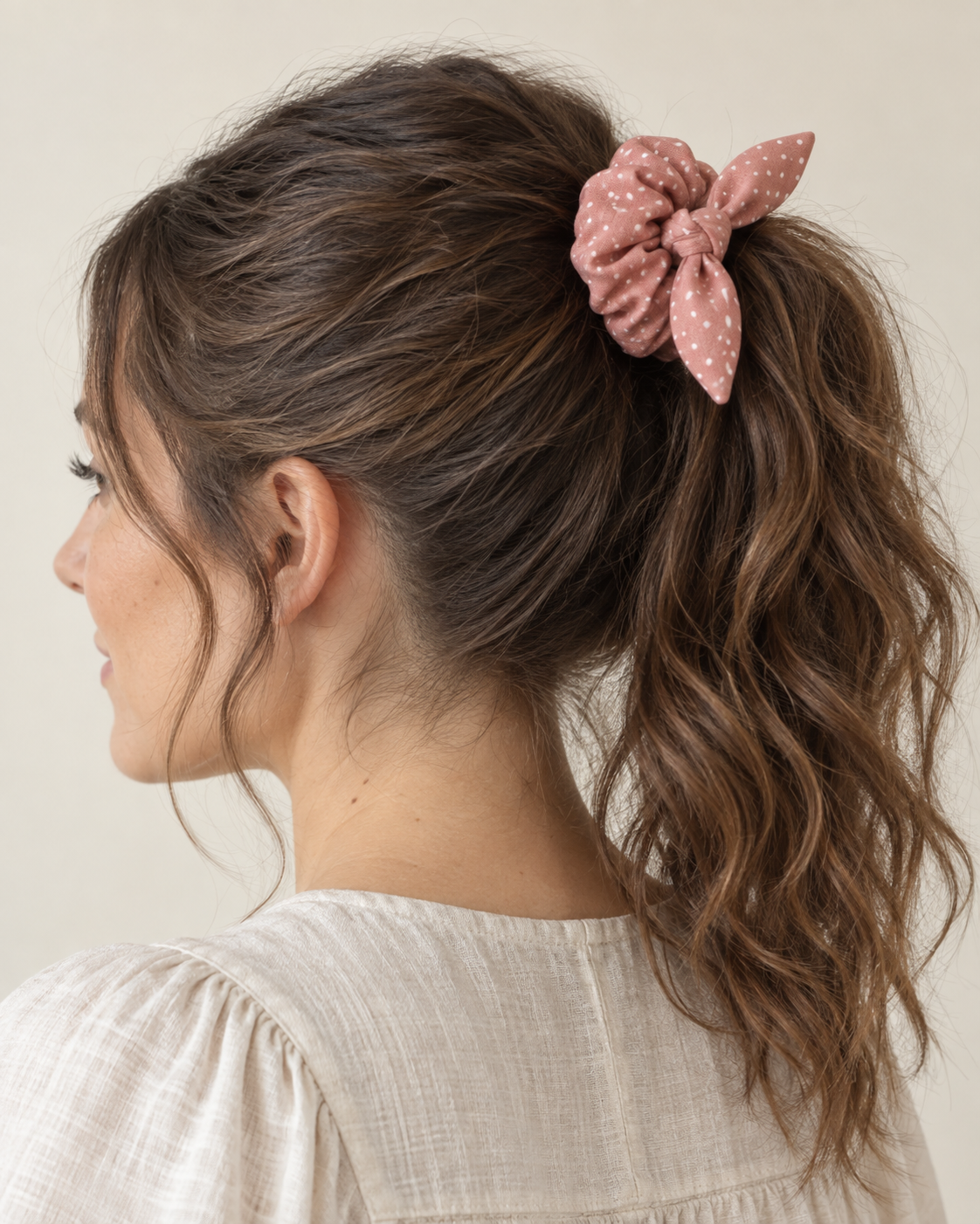 Design preview: adult woman wearing a dusty rose dotted hair scrunchie with a removable short knotted bow, three-quarter view