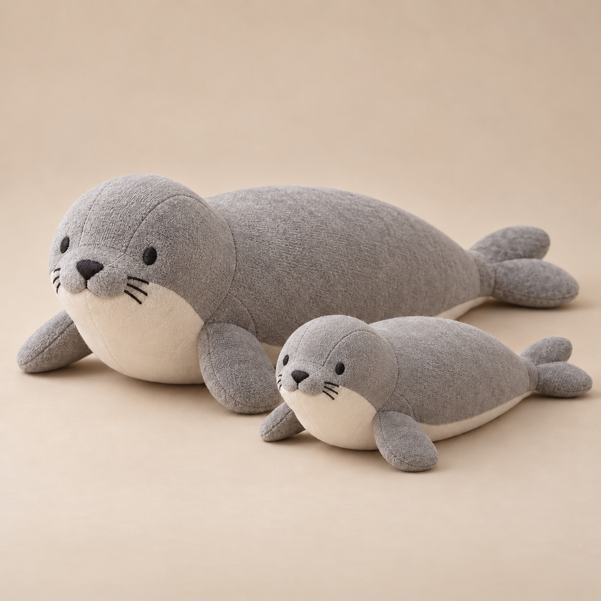 Gray harbor seal plush and smaller pup with ivory bellies, embroidered faces and rounded flippers