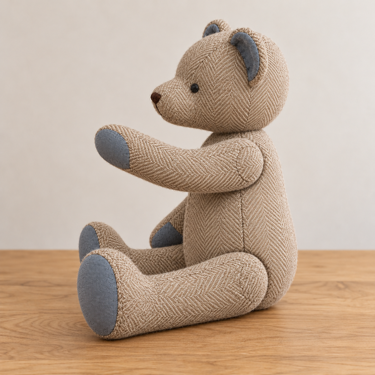 Side view of the herringbone keepsake teddy bear with one arm raised at its shoulder joint