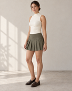 Three-quarter design preview of the olive pleated mini skirt, showing the contoured button yoke and crisp pleated hem