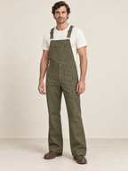 Man wearing coordinated olive bib overalls with angular bib pocket and side-button openings