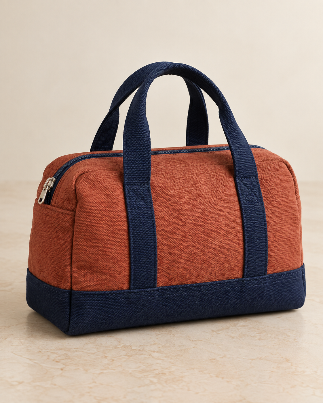 Design preview: rust and navy mini duffel with two short carrying handles, a separate lower band and closed top zipper