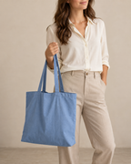 Design preview: adult woman holding a soft blue pack-away tote by its two flat handles, with a plain exterior and open top