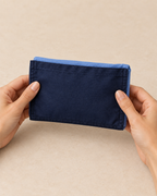 Design preview: same blue tote folded into its attached navy pocket, held as a compact two-tone fabric packet