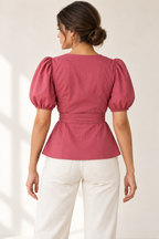 AI design preview: raspberry puff-sleeve wrap blouse on an adult woman, back view showing closed back and smooth waist sash.