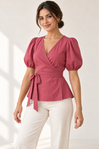 AI design preview: raspberry puff-sleeve wrap blouse on an adult woman, three quarter view showing V crossover neckline and matching waist ties.