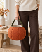 AI design preview: adult woman holding the orange pumpkin treat bag beside her leg by its single short olive fabric handle.