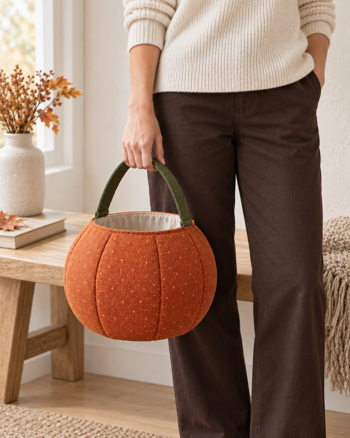 AI design preview: adult woman holding the orange pumpkin treat bag beside her leg by its single short olive fabric handle.