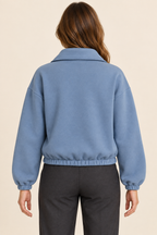 AI preview: plain rear of the dusty-blue knit pullover with folded collar and matching fabric elastic wrist and waist casings.