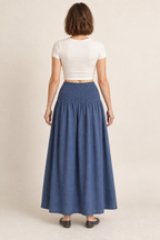 AI design preview: rear view of the same muted-indigo maxi skirt showing continuous shirring around the yoke and a plain closed ankle-length skirt