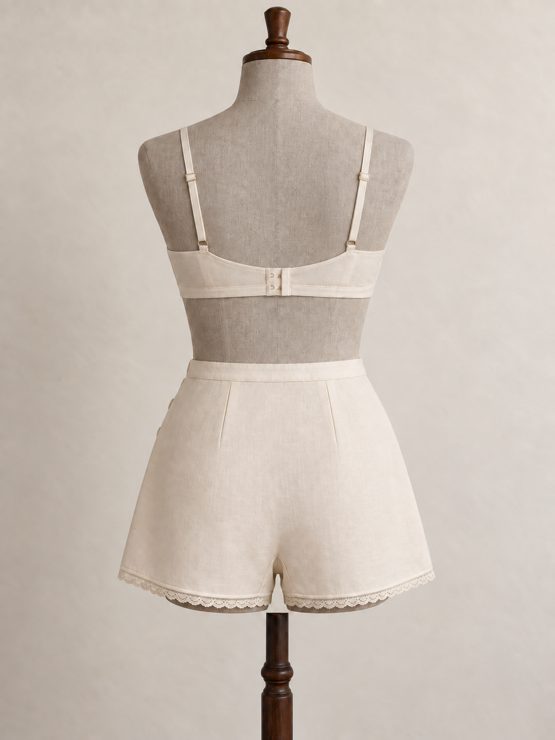 Back view of an ivory 1930s-inspired bra and matching tap pants on a grey linen-covered fitting mannequin.
