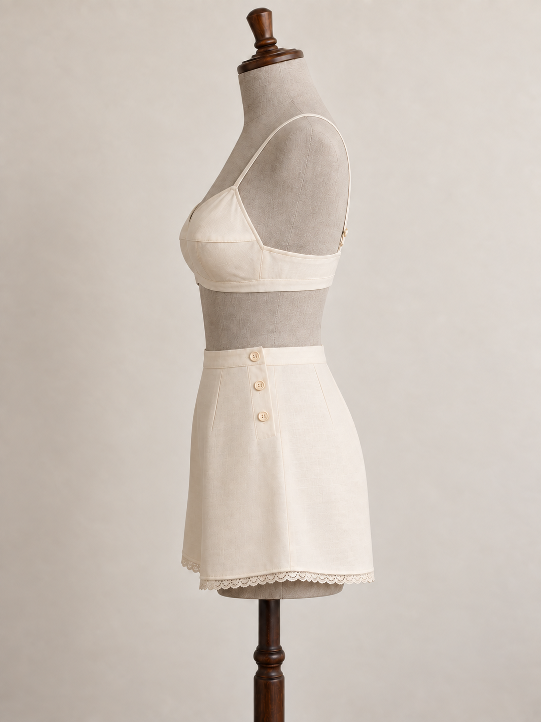 Left-side view of an ivory bra and side-button tap pants set on a grey linen-covered fitting mannequin.