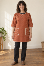 Rust sprig-print sleeved smock apron with two bound patch pockets on a woman