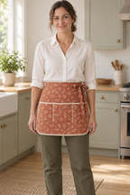 Design preview: adult woman wearing a terracotta botanical half apron with three front pockets and ivory-bound rounded corners.