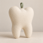 Plain ivory back of the tooth-shaped keepsake pillow showing blanket-stitched edges and sage hanging loop