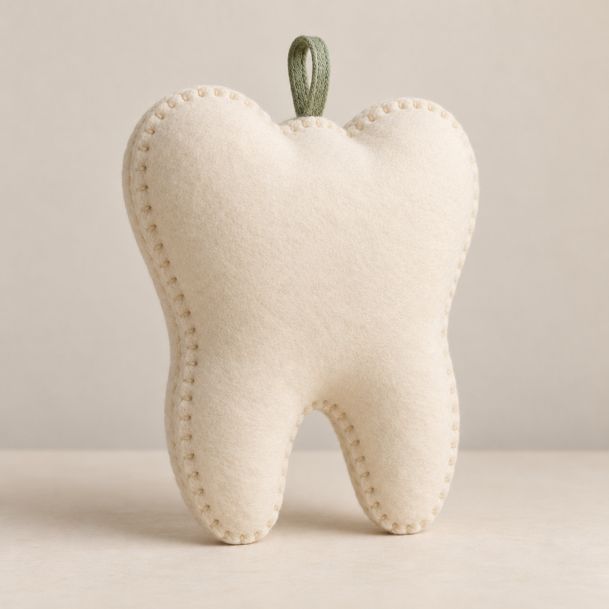 Plain ivory back of the tooth-shaped keepsake pillow showing blanket-stitched edges and sage hanging loop
