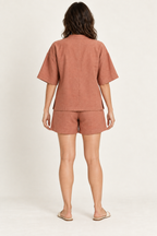 AI design preview: same woman and terracotta lounge set from behind, showing plain center-back top seam, elbow sleeves and loose shorts