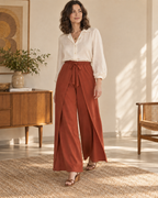 Front view of rust-red wrap-and-tie wide-leg trousers with overlapping leg panels and a front bow