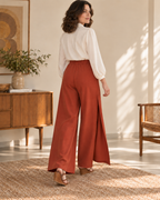 Rear view of rust-red wrap trousers showing the gathered waist casing and two wide full-length legs